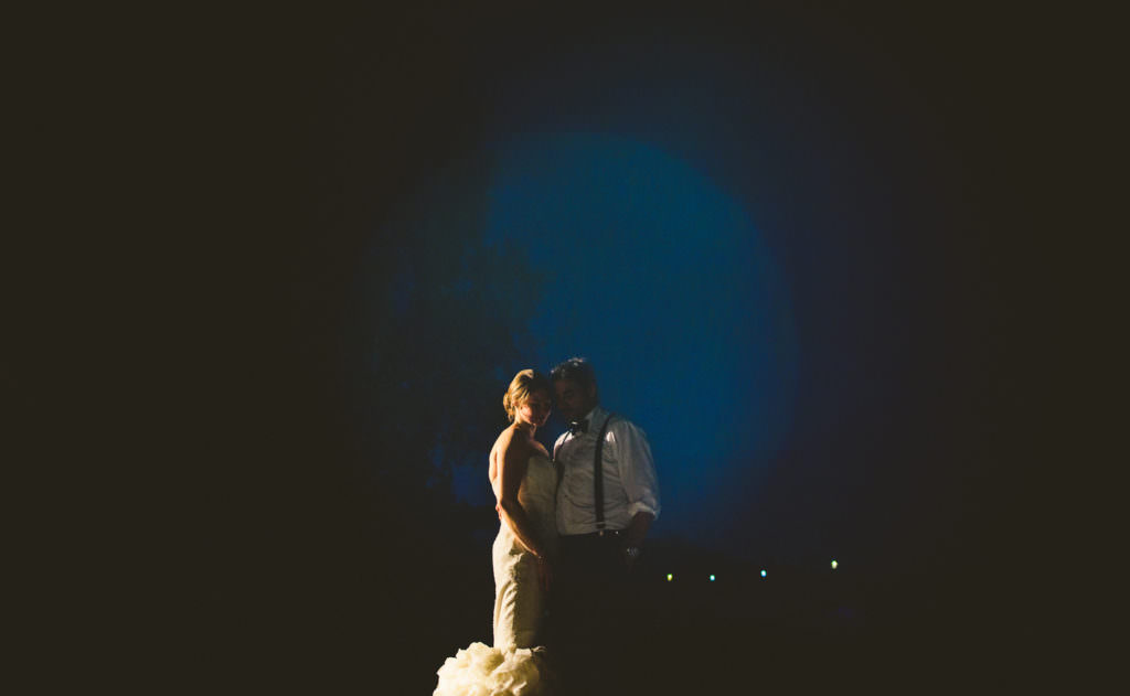 night portrait of wedding couple in blue bubble lit by car headlights